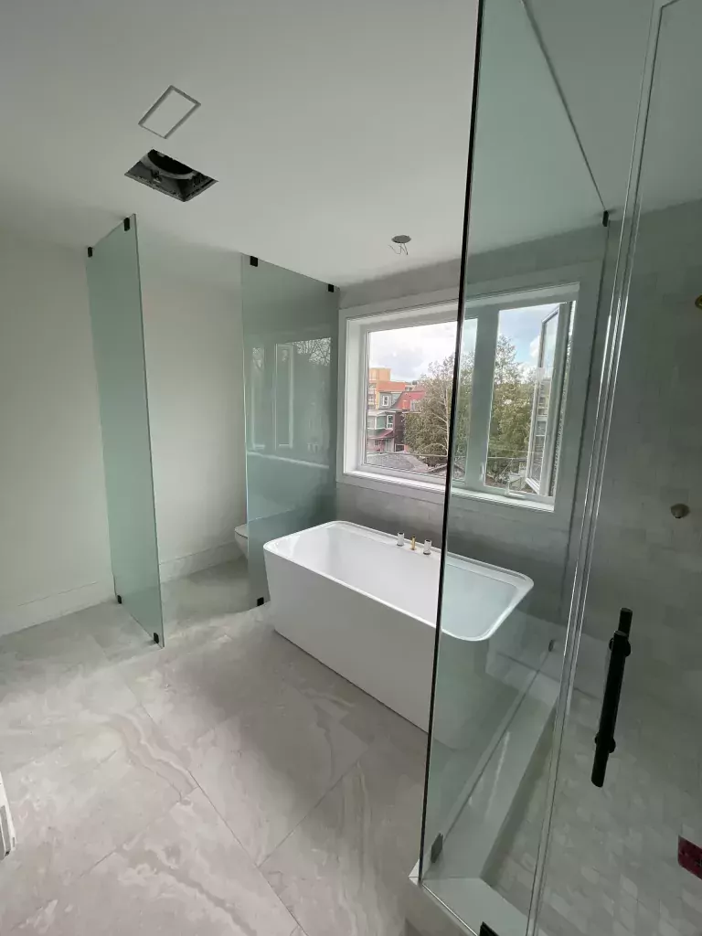 Tall clear glass shower door with a dark vertical handle in a bright bathroom