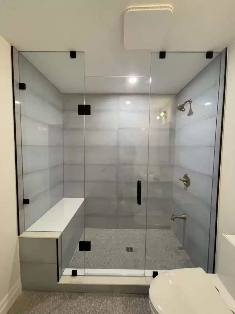 Wide frameless inline shower door and fixed glass panels with dark hardware