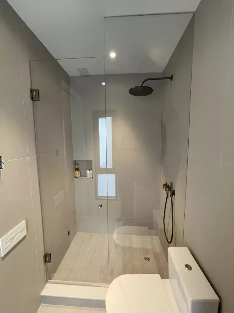 Clear hinged shower door and fixed panel with black hardware in a compact bathroom